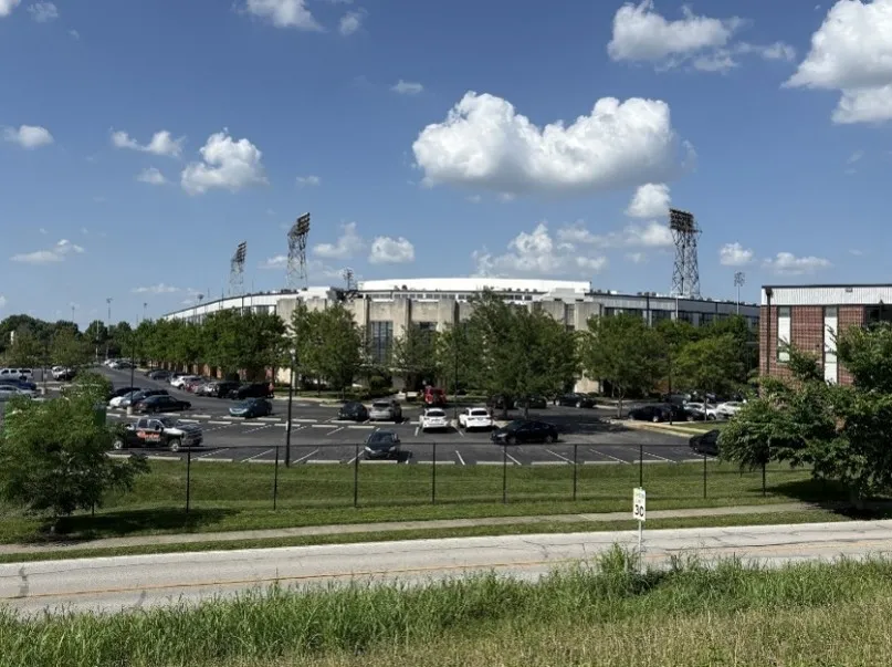 Three stadium lights stand above the main entrance to Stadium Lofts, which is partially obscured by trees